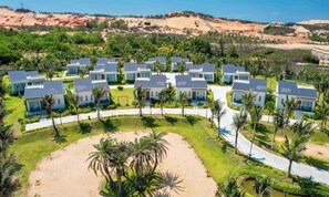 Ein Resort mit mehreren modernen Villen, einem zentralen Weg und einer Sandfläche mit Palmen.