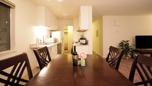 A dining area with a wooden table, chairs, a bottle of wine, and a vase of flowers.