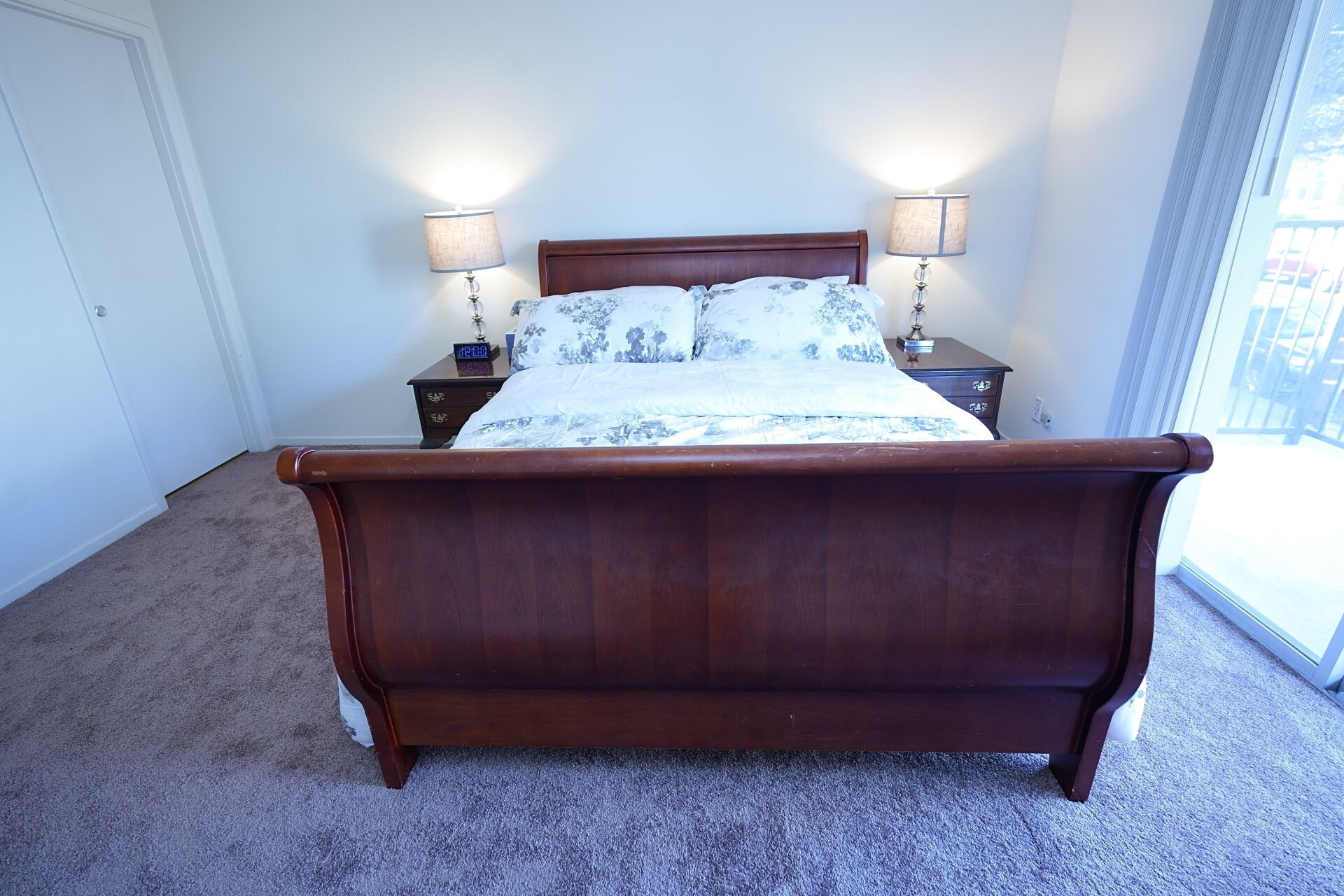 Un dormitorio con cama de madera, dos mesitas de noche con lámparas, una mesita auxiliar y una ventana con vistas.