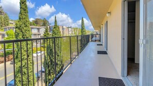A balcony with a metal railing, a door leading to a room, and a view of neighboring houses and trees.