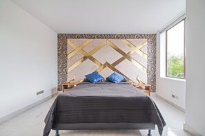 A modern bedroom with a geometric-patterned headboard, a large bed with a dark grey bedspread, and two blue pillows. - 2bedroom with pooltable 1 block -Lleras  (Medellín)