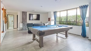Un salon moderne avec une table de billard, un canapé et une grande fenêtre agrémentée de rideaux.