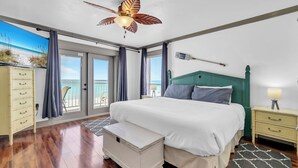 Ein Schlafzimmer mit einem großen Bett, einem Deckenventilator, einem Nachttisch, einer Kommode und Meerblick durch das Fenster.
