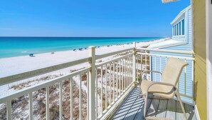 Ein Balkon mit Blick auf einen Strand, ein Stuhl und ein Gebäude mit blauer Schrägverkleidung.