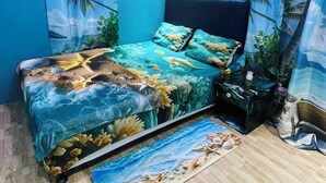Une chambre à coucher avec un lit, une table de chevet et des rideaux ornés d’un motif représentant une plage tropicale.