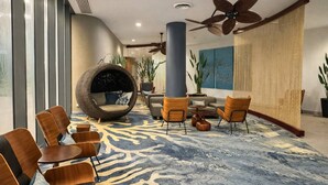 A modern lobby with a large, round, wicker chair, wooden chairs, a blue patterned carpet, and a ceiling fan. - Cairns Harbour Haven | Marina Views | Pool & Spa | near Reef Terminal (Cairns City)