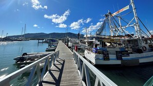 A pier with boats docked, a fishing boat with a net, and a sign for 'Fresh Seafood'. - Cairns Harbour Haven | Marina Views | Pool & Spa | near Reef Terminal (Cairns City)
