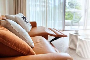 Ein stilvoller Lounge-Bereich mit Ledersofas und einem runden Tisch, mit einem großen Fenster und Blick auf Grünflächen.