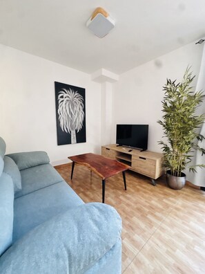 A living room with a sofa, a coffee table, a TV stand, and a potted plant. - Holiday Apartment Gara (Adeje)