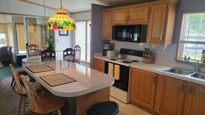 A kitchen with wooden cabinets, a central island with stools, a microwave, a stove, and a hanging fruit-themed light fixture. - Cozy 2 bedroom Lake Cottage on Lamoka Lake in Bradford New York (Bradford)