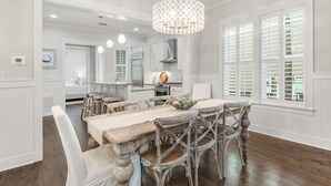A dining area with a wooden table and chairs, a chandelier, and a view of the kitchen and dining room through large windows. - 🎨 WaterColor ~ Golf Cart | Bikes | Private Beach | 4 Heated Pools & Lazy River (Watercolor)