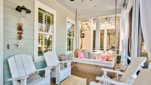 A porch with white Adirondack chairs, a swing, and a hanging light fixture. - 🎨 WaterColor ~ Golf Cart | Bikes | Private Beach | 4 Heated Pools & Lazy River (Watercolor)