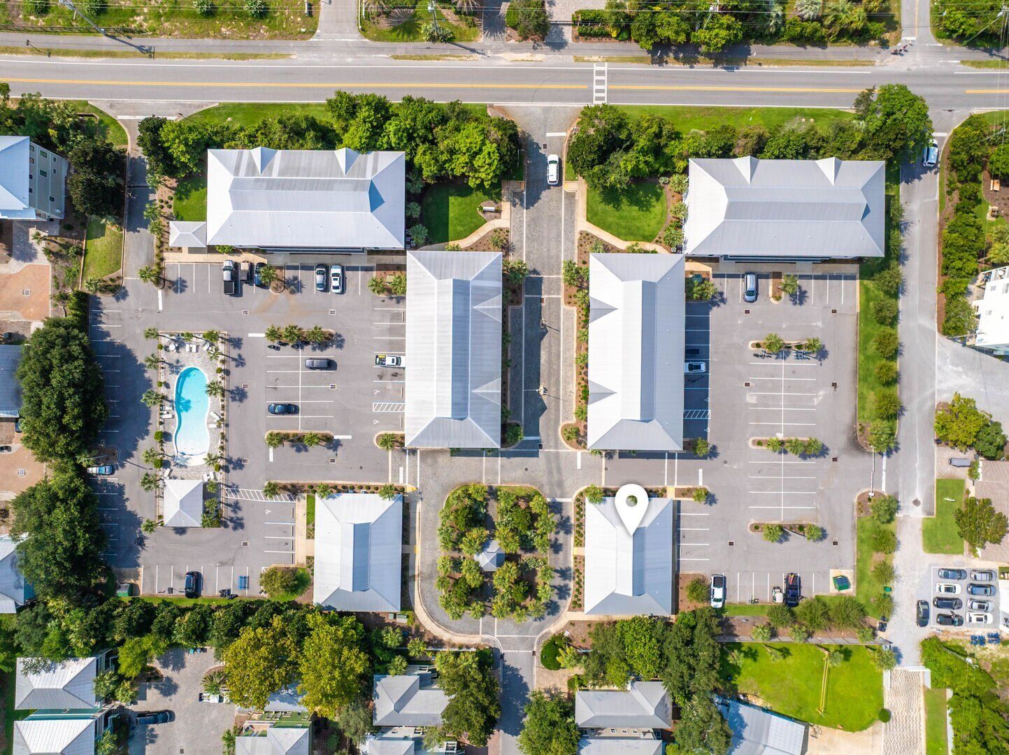 Vista aérea de un estacionamiento con varios edificios, una piscina y zonas verdes circundantes.