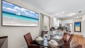 Un coin repas avec une table ronde, des fauteuils en cuir et un grand tableau représentant une scène de plage.