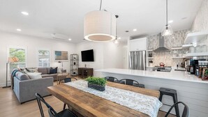 Una cocina moderna con una isla central, un comedor con mesa de madera y una sala de estar con sofá.
