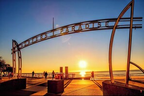 A metal archway with the words "SURFERS PARADISE" against a sunset backdrop.