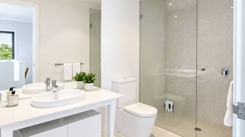 A modern bathroom with a white vanity, two sinks, a toilet, and a glass-enclosed shower.