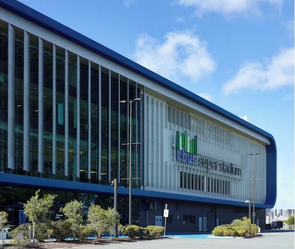 A modern building with a large glass facade, a prominent 'cbus superstore' sign, and a parking lot with trees.