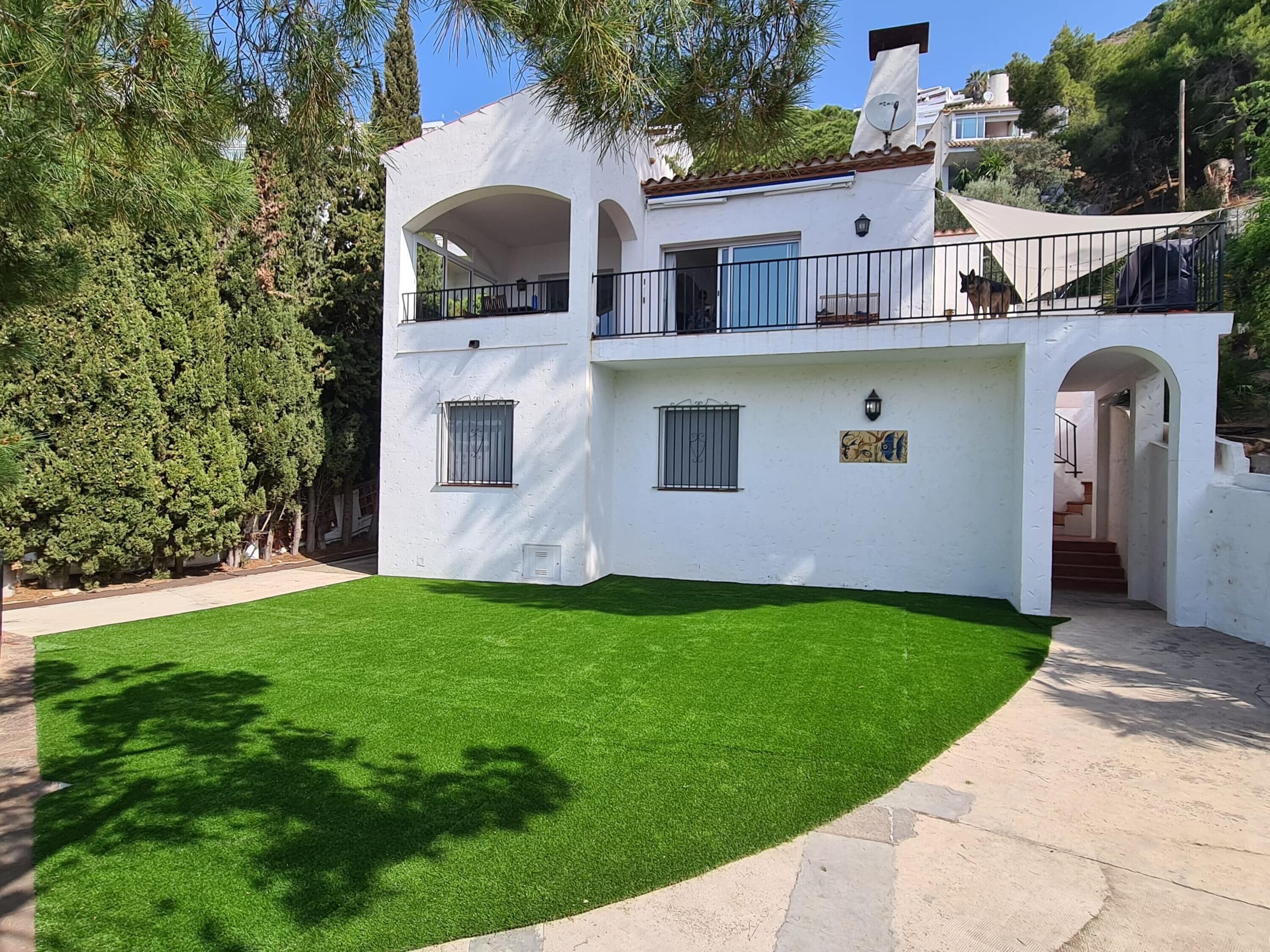 A two-story white house with a balcony, a well-maintained lawn, and a satellite dish.