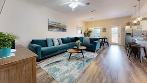 Un salon spacieux avec un canapé de couleur turquoise, une table basse en bois et un ventilateur de plafond.