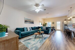 A spacious living room with a teal sofa, wooden coffee table, and a ceiling fan. - Boardwalk, Shared Pool, Parking for 5 (Port Aransas)