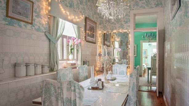 A dining area with a table set for two, surrounded by chairs with floral upholstery. There are white ceramic jars on the wall to the left, and a chandelier hangs from the ceiling. -  6 BR/3BA Gorgeous, Historic, Charming, Trolley, French Quarter, Sleeps 12 (Metairie)