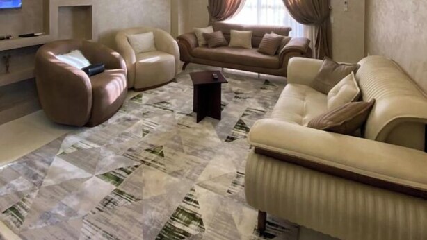 Una sala moderna con un conjunto de sofá, un sillón tipo puff, un televisor de pantalla plana y una alfombra estampada.