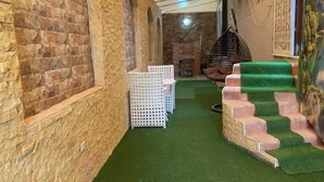 Un pasillo con paredes de piedra, alfombra verde, sillas de plástico blanco y una escalera con escalones verdes.