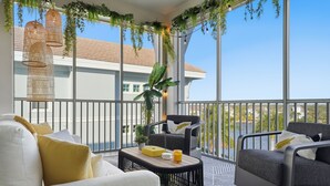 A balcony with a sofa, armchair, and table, decorated with plants and hanging lights. - One Particular Penthouse | Top-Floor Condo at Margaritaville Near Anna Maria Island (Bradenton)