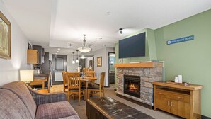 Un salon avec une cheminée, un coin repas et un téléviseur fixé au mur.
