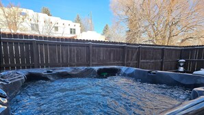 Un bain à remous entouré d’une clôture en bois, avec un bâtiment visible au fond.