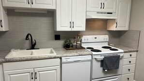 A kitchen with white cabinets, a white dishwasher, a stove, and a sink. - Convenient & Cozy condo on 400 (Logan)