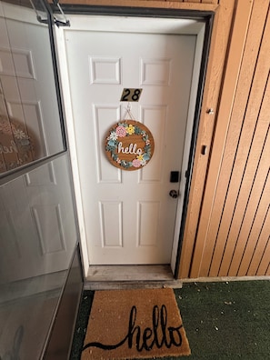 A white door with a 'hello' sign, a number '28' sign, and a 'hello' doormat.