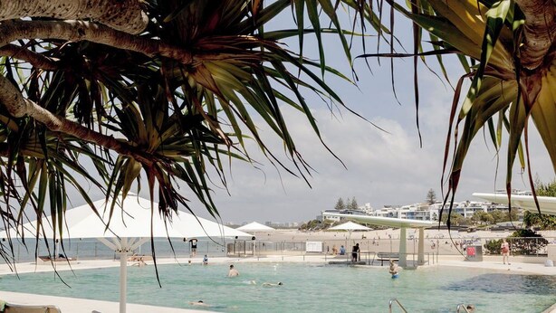 Zona de piscina con sillas de descanso, un puesto de socorristas y vista a la playa y al océano.