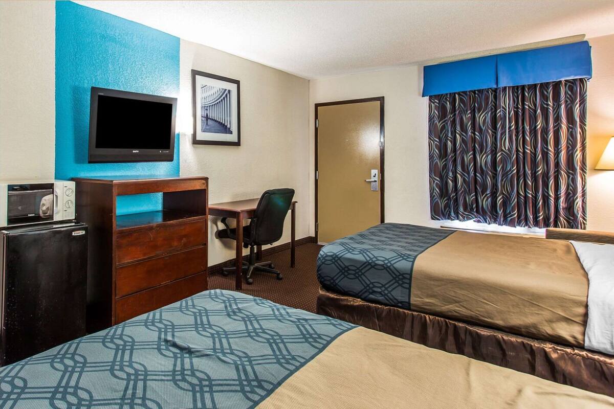 Habitación de hotel con dos camas, un escritorio, una silla, un televisor y una puerta.
