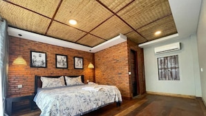 Een slaapkamer met een bakstenen muur, een bed met bloemenbedekking, een houten vloer en een plafond met een geweven patroon.