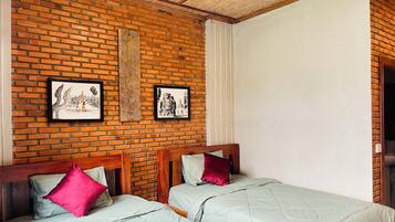 Una habitación con pared de ladrillo, dos camas con cabeceros de madera y una obra de arte en la pared.
