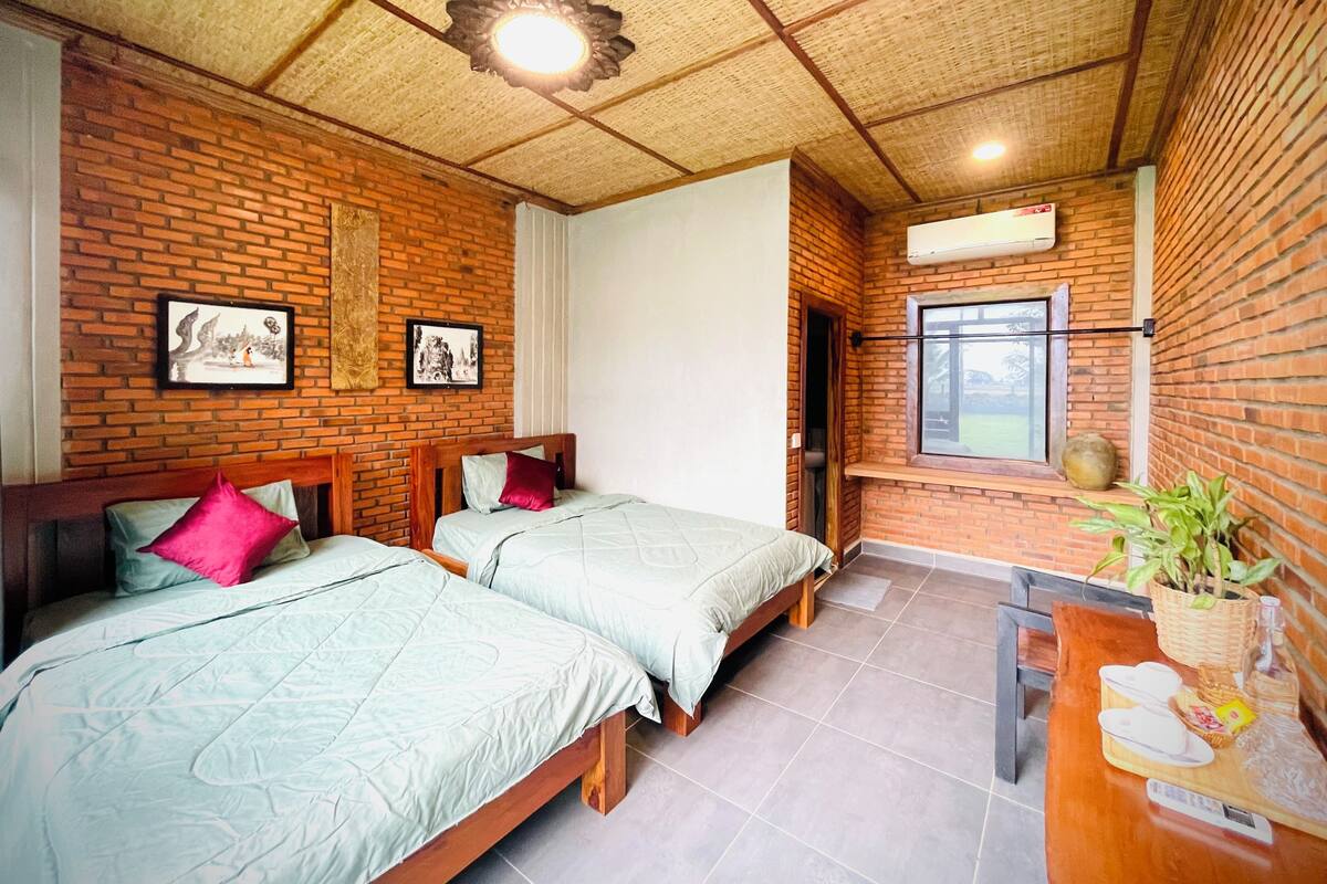 A room with two beds, a wooden headboard, a brick wall, a ceiling fan, and a window.