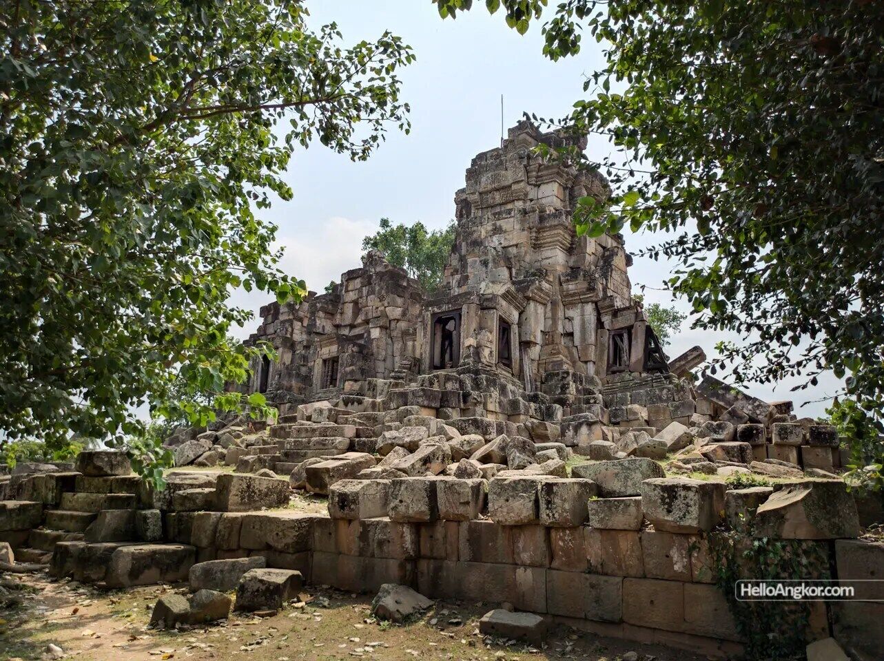 An ancient stone structure with multiple levels and a central tower, surrounded by overgrown vegetation.