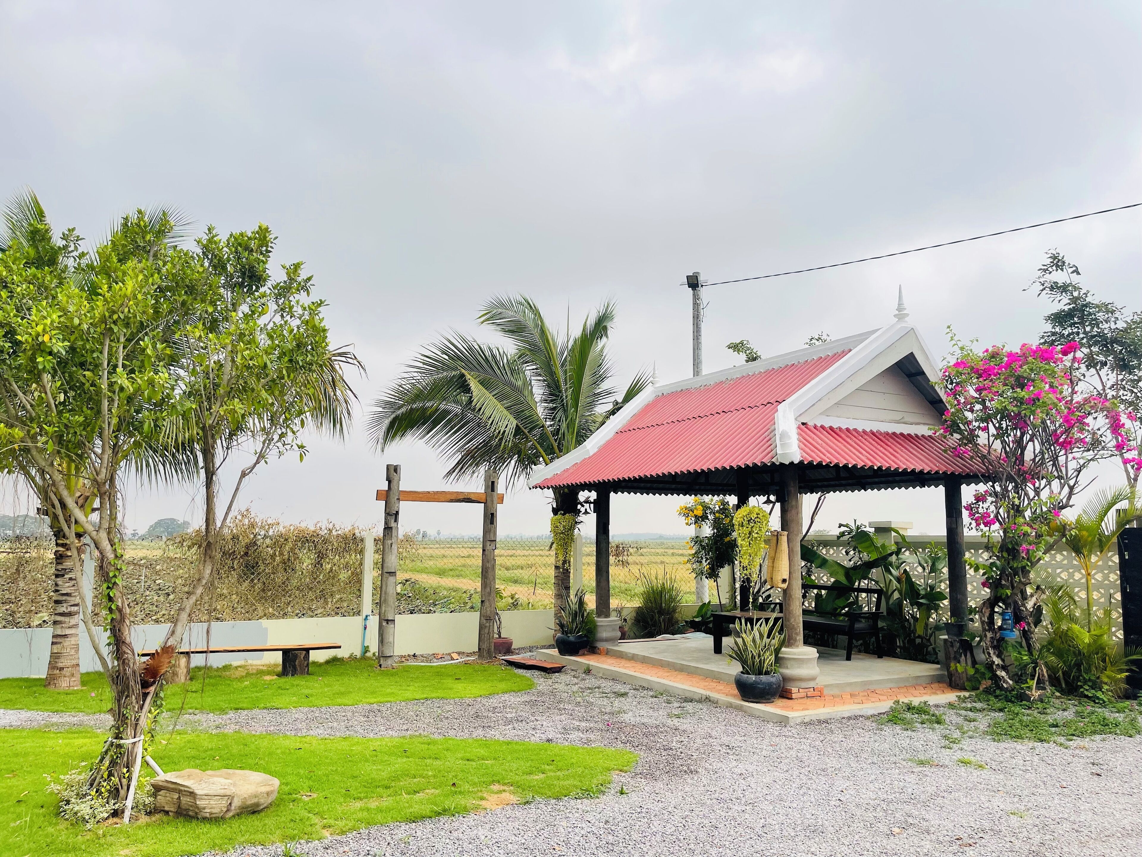 A covered outdoor area with a red roof, surrounded by greenery and a fence.