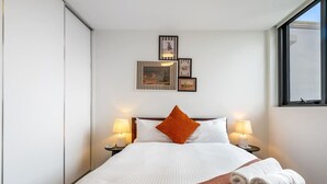 Una habitación de hotel con cama, dos lámparas de noche, una ventana y cuadros en la pared.