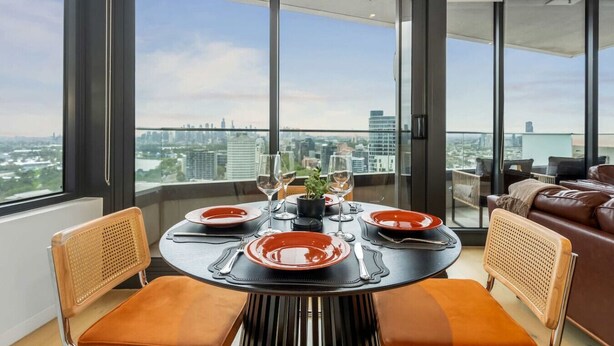 Un comedor con una mesa dispuesta para dos personas, ventanas amplias y vistas a la ciudad.