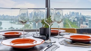 Una mesa lista para comer con vista a la ciudad, una planta en maceta y cielo despejado.