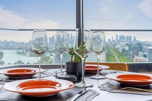 A table set for dining with a city view, a potted plant, and a clear sky. - Urban Cowboy Loft | Skyline Views, Pool & Parking (St Kilda)