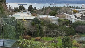 A view from a balcony overlooking a cityscape with multiple ships on the water, a variety of buildings, and a well-maintained garden area. - Beachside Retreat Paradise w Pool & Pickleball Court — 5 mins to downtown (Vancouver)