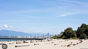 A beach with a city skyline in the background, large rocks on the sand, and a clear sky. - Beachside Retreat Paradise w Pool & Pickleball Court — 5 mins to downtown (Vancouver)