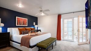 Une chambre à coucher comprenant un lit, des tables de chevet, un ventilateur de plafond, une fenêtre et une porte donnant sur un espace extérieur.