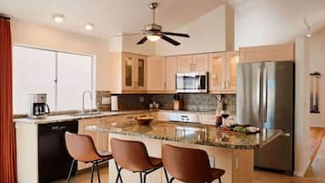 Una cocina moderna con una isla central, taburetes de bar, microondas, refrigerador y ventilador de techo.