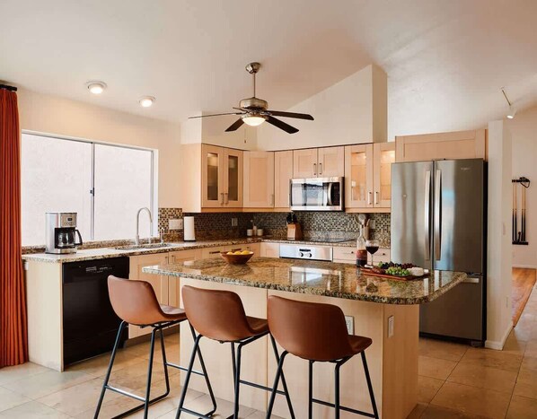 Una cocina moderna con una isla central, taburetes de bar, microondas, refrigerador y ventilador de techo.