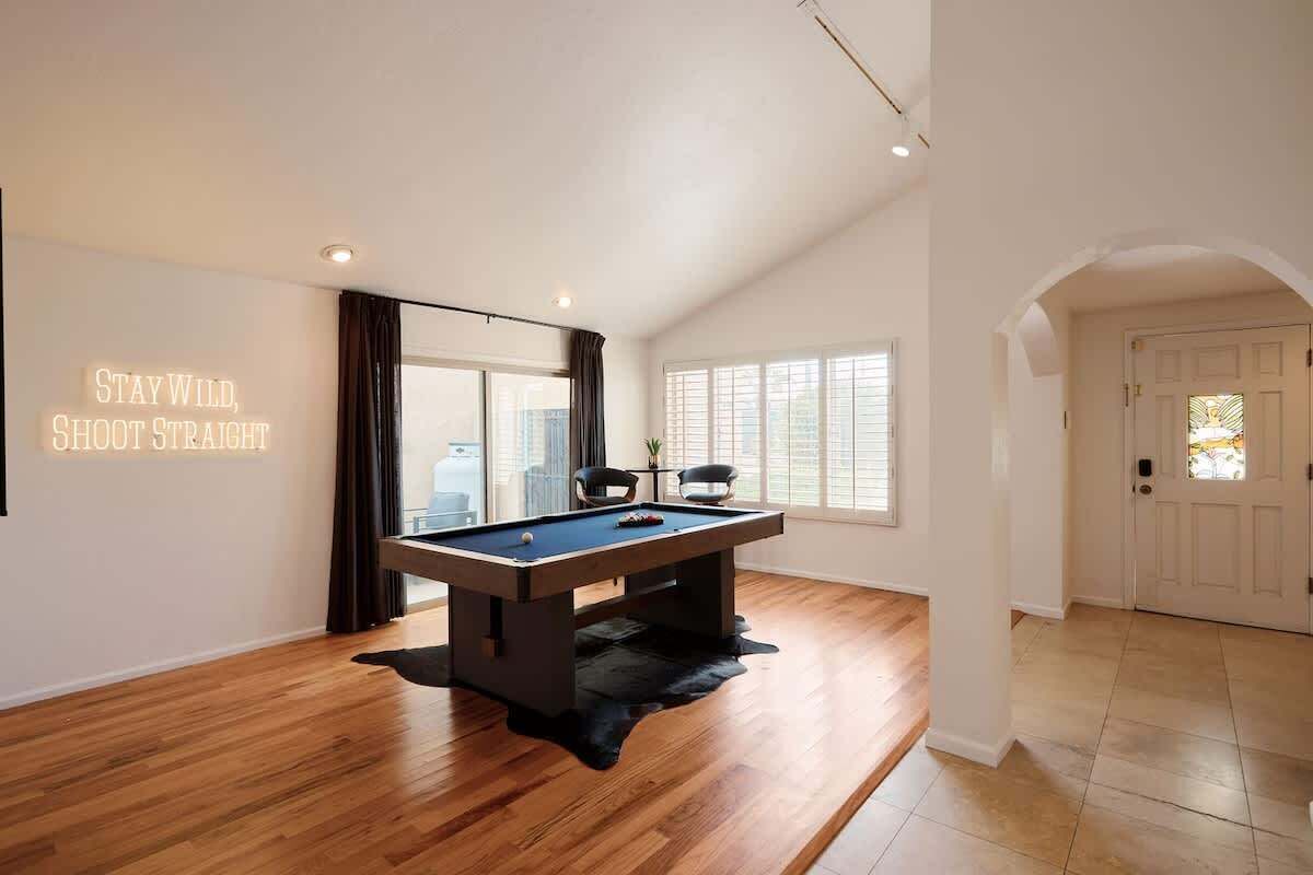 A modern room with a pool table, a motivational quote on the wall, and a view through a large window.